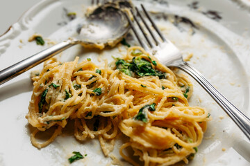 Spaghetti in creamy spinach sauce with cheese, on a messy floral plate with silver fork and spoon, half eaten, close up