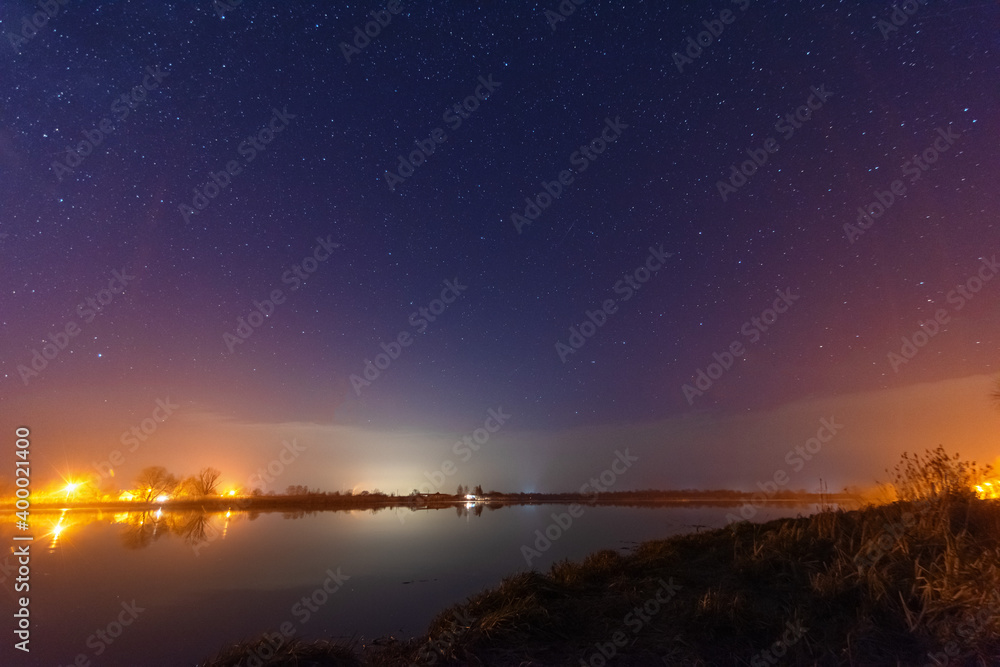 Wall mural a magical starry night on the river bank with a large tree and a milky way in the sky and falling st