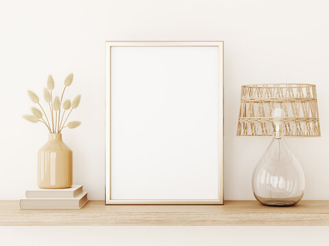 Vertical poster art mockup with gold metal frame, dried grass in vase, wicker lamp and books on empty warm beige wall background. Boho interior decoration. A4, A3 format. 3d rendering, illustration