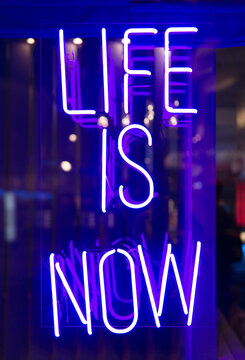 Neon glowing sign 'life is now' in a cafe window.