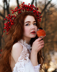 Beautiful red haired girl in wedding dress with bullfinch birds on hands