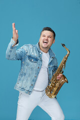 happy musician man with the saxophone on blue studio background. Music concept.