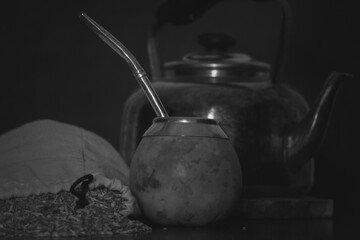 Black and white shot of a brown calabash, a kettle and a bag filled with tea herb called mate