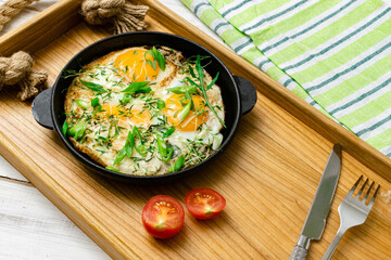 scrambled eggs with sprouts of greens and green onions in a frying pan on a wooden tray. Morning breakfast.