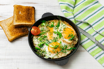 scrambled eggs with greens sprouts and green onions in a pan on a wooden background.