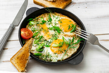 scrambled eggs with greens sprouts and green onions in a pan on a wooden background.