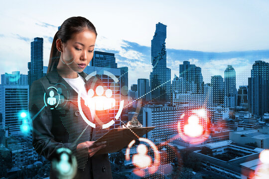 Attractive Asian HR director at international company is looking into personal organizer to plan business meeting to recruit highly qualified specialists. Social media icons over Bangkok.