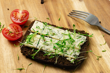 Rye bread with blue cheese and sprouted grains on a wooden background.