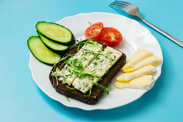 Rye bread with blue cheese and sprouted grains and tomatoes on a plate on a blue background.