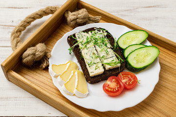 Blue cheese sandwich, brie cheese, cucumber and tomatoes on a plate on a wooden tray. Healthy food.