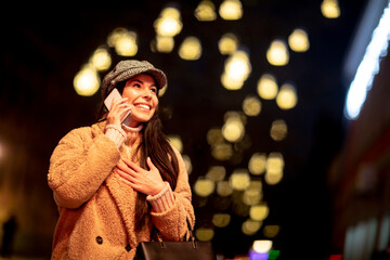 Pretty young woman using her mobile phone in the street at Christmas time