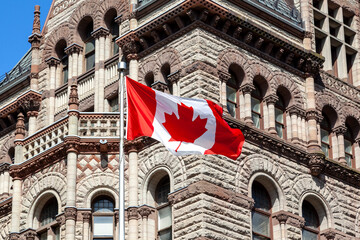 The waving Canadian flag with Old City Hall in background in Toronto, Canada. Toronto is the...