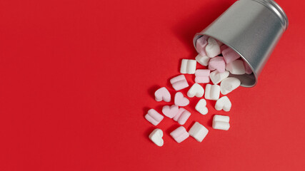 sweets-pink and white marshmallows in the shape of hearts fell out of a tin bucket on a red background. congratulations on Valentine's Day. flat lay, copy space