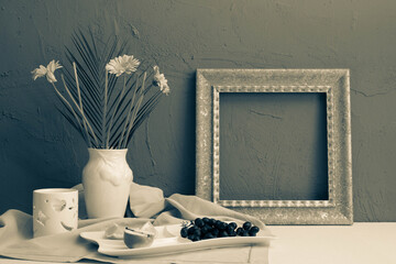 black and white photo, frame for a picture, a cup with coffee and a teapot and a vase with gerbera flowers, grapes and oranges on a blue background