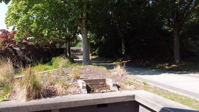 aerial panout through modern concrete archway of cultic ceremonial grounds in a downtown modern city park on a hot sunny summer day next to pedestrian cyclist pathway and by an unmanaged garden greens