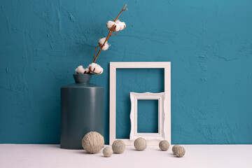 Fototapeta na wymiar white cotton in a vase, photo frames on a blue background and decor