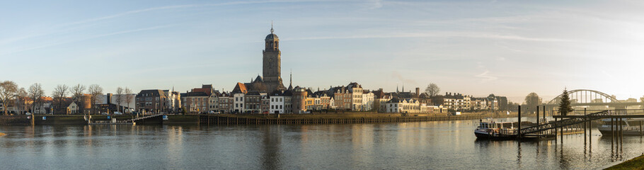 Fototapeta na wymiar Super wide cityscape panorama of the Dutch Hanseatic medieval city of Deventer in The Netherlands seen from the other side of the river IJssel at sunrise