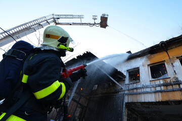 A firefighter with a mask and a fire platform extinguishes a huge fire in an industrial building with thick black smoke
