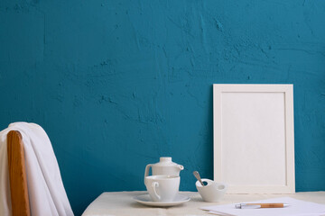 pen and piece of paper, back of a chair, white photo frame, cup and teapot with coffee on a blue background
