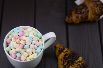 morning breakfast with a mug of coffee and marshmallow, and a chocolate croissant on a wooden board