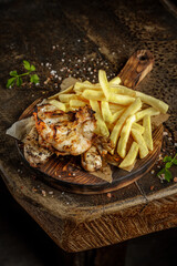 Grill house concept. Grilled, roasted, fried tasty chicken meat with french fries on the old wooden cutting board.