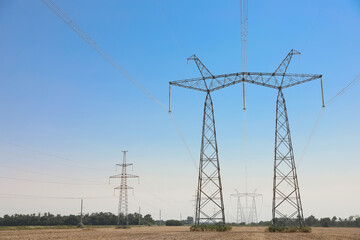 High voltage towers with electricity transmission power lines in field on sunny day