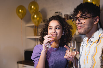 happy hispanic woman drinking champagne near friend during party