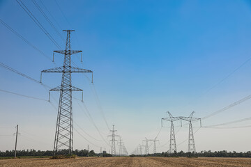 High voltage towers with electricity transmission power lines in field on sunny day