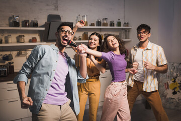 happy hispanic woman dancing with friends and holding microphone near man singing karaoke