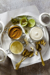 different types of sauces in glass jars. with pistachios, cashews and vegan mayo on a stone background