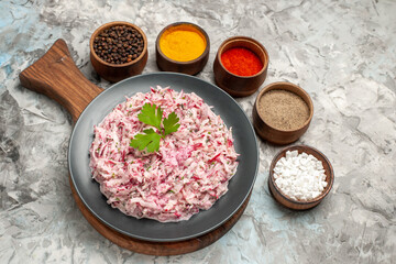 Front close view of tasty chicken salad with mayonnaise and beet served with green on brown wooden cutting board and different spices