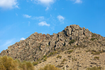 Natural rocky hill in daylight, plants and clear blue sky in the background.