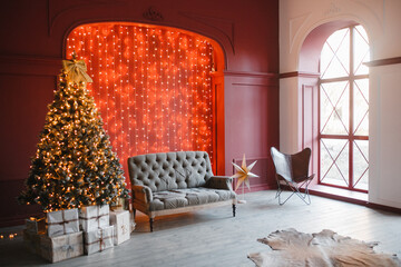 Christmas and New Year decorated interior room with light bokeh garland and New year tree and classic grey sofa in front of red wall. Loft trend interior
