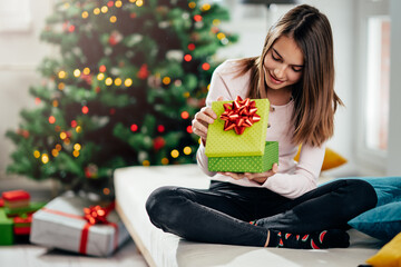 A cheerful girl opens a gift at the Christmas tree.