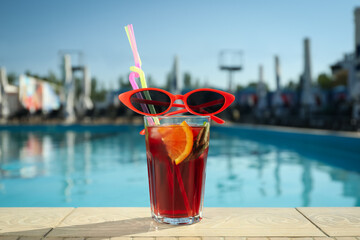 Tasty refreshing cocktail and sunglasses on edge of swimming pool. Party items