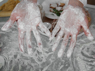 The woman shows her palms sprinkled with flour. A woman is preparing Christmas cookies. Close-up of female palms on the background of the kitchen table with homemade cookies