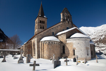 Fototapeta na wymiar Horizontal exterior view of the Romanesque Santa María church with its apse and graveyard covered by snow in Artíes, Vall d’Aran, Lleida, Spain