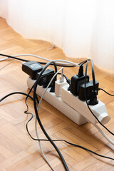 Messy outlet power extension cord on an apartment wood tile floor with various charging devices...