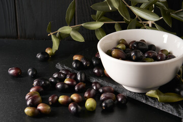 A group of green and black olives photographed on a black stone table and a background of black wooden planks. The olives have just been picked from the olive tree.