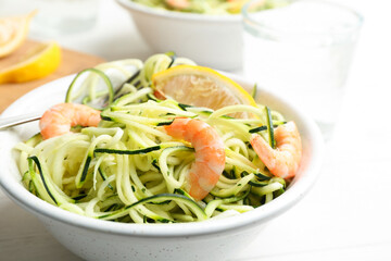 Delicious zucchini pasta with shrimps and lemon in bowl on white table, closeup
