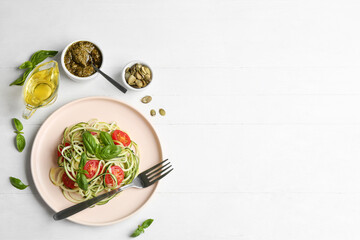 Delicious zucchini pasta with basil and cherry tomatoes served on white wooden table, flat lay. Space for text