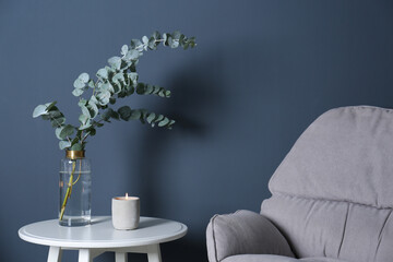 Beautiful eucalyptus branches and burning candle on white table near blue wall. Interior element