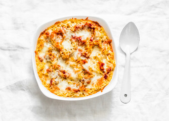 Roasted orzo pasta with tomato sauce and mozzarella in a baking dish on a light background, top view