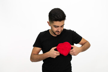 Young male model holding a heart-shaped gift box in his hand. He is wearing a black shirt. Isolated pattern and white background.