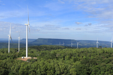 Wind-powered turbines are installed in the center of the green forest.  The picture shows a clear sky and a lush forest.