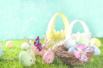 Happy Easter background, spring-time concept. Colorful pastel eggs, nests and bunny toys on  sunny spring day, meadow green grass. Easter greeting card mockup, copy space.