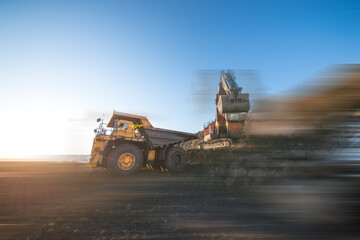 Obraz premium Big dump trucks and excavator in coal mine at sunrise 
