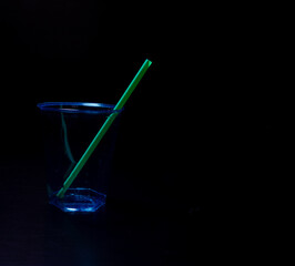 Green drinking plastic straw in a plastic cup on a black background.