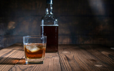 glass of whiskey with ice cubes on rustic wooden table, copy space on dark background