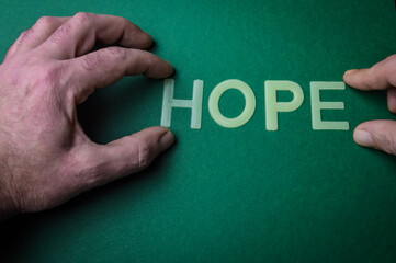 Human fingers holding the word hope written with plastic letters on green paper background, concept